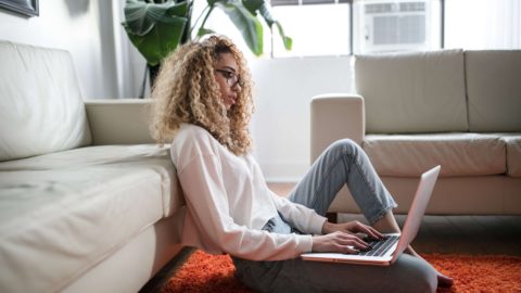 A curly hair woman sitting down searching online on a laptop -cash your opinions