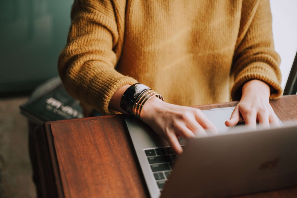 A person sitting down working on a laptop with a brown sweater