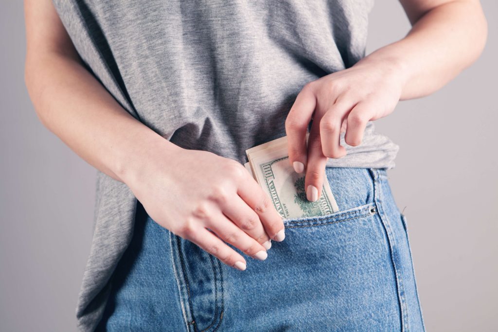 A woman in gray shirt and jeans putting money in her pocket