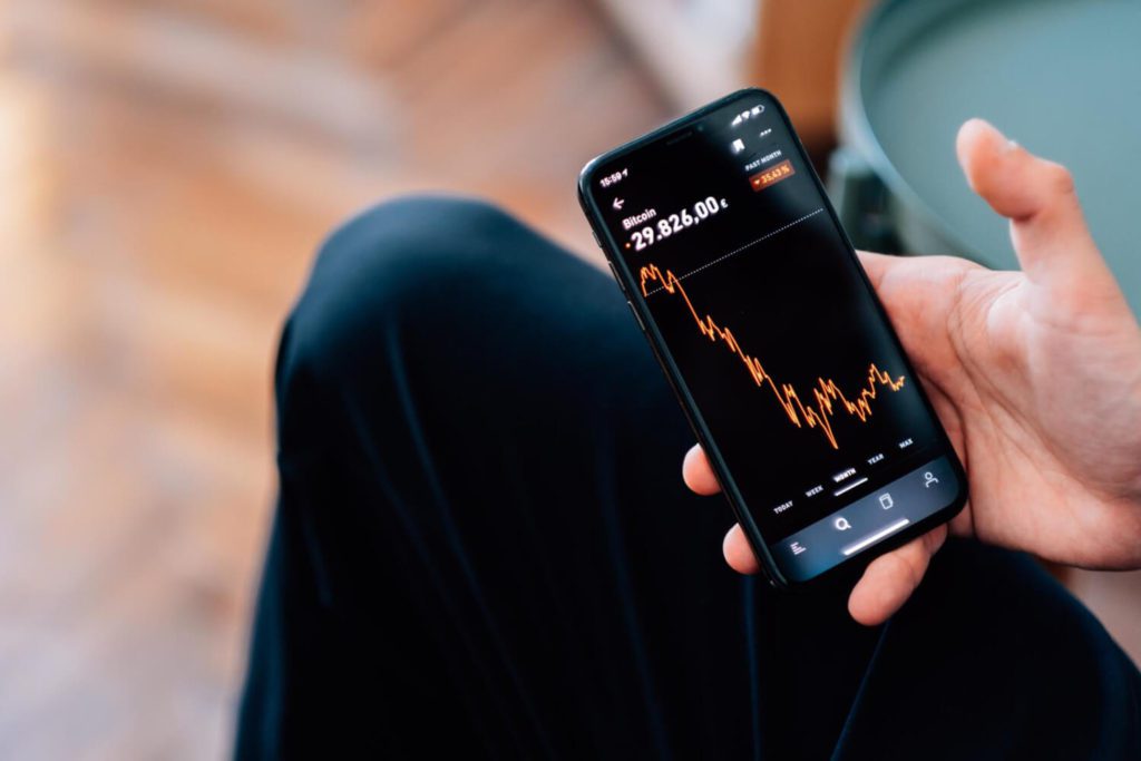 A person holding a smartphone with an investment app interface on the screen, depicting the convenience and accessibility of investing in the digital age.