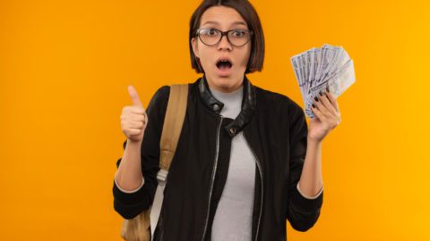 impressed student girl, glasses, backpack, holding money, thumbs up, Crypto Future, orange background